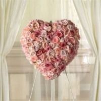 Heart-shaped arrangement of pink roses on a stand, in front of sheer curtains