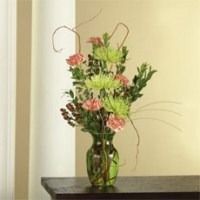 Green vase with a mixed bouquet of pink and green flowers on a dark table