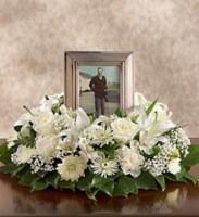Framed portrait surrounded by white floral arrangement on a wooden table