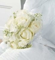 White rose bridal bouquet with soft green accents on a white fabric background