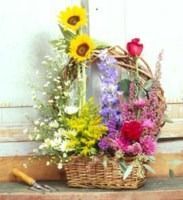 Basket of colorful flowers with sunflowers, roses, and purple blooms on a rustic table