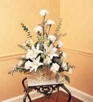 White floral arrangement on a decorative metal stand against a beige corner wall.