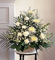 Large white and pale yellow floral arrangement with greenery on a small stand indoors