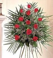 Red flower and green palm-leaf bouquet in a vase against a light wall