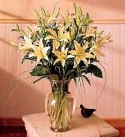Bouquet of white and yellow lilies in a glass vase on a table, with a small black bird figurine nearby