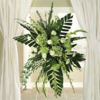White and green floral arrangement with long leaves and cascading greenery on a stand, framed by white drapes