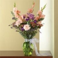 Pink and purple flower arrangement in a green vase with a white ribbon on a table
