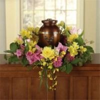 Floral arrangement with yellow and pink flowers around a bronze urn on a wooden mantel