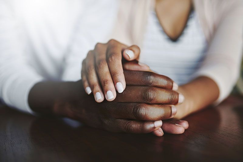 Hands clasped together on a table, one resting gently over the other.