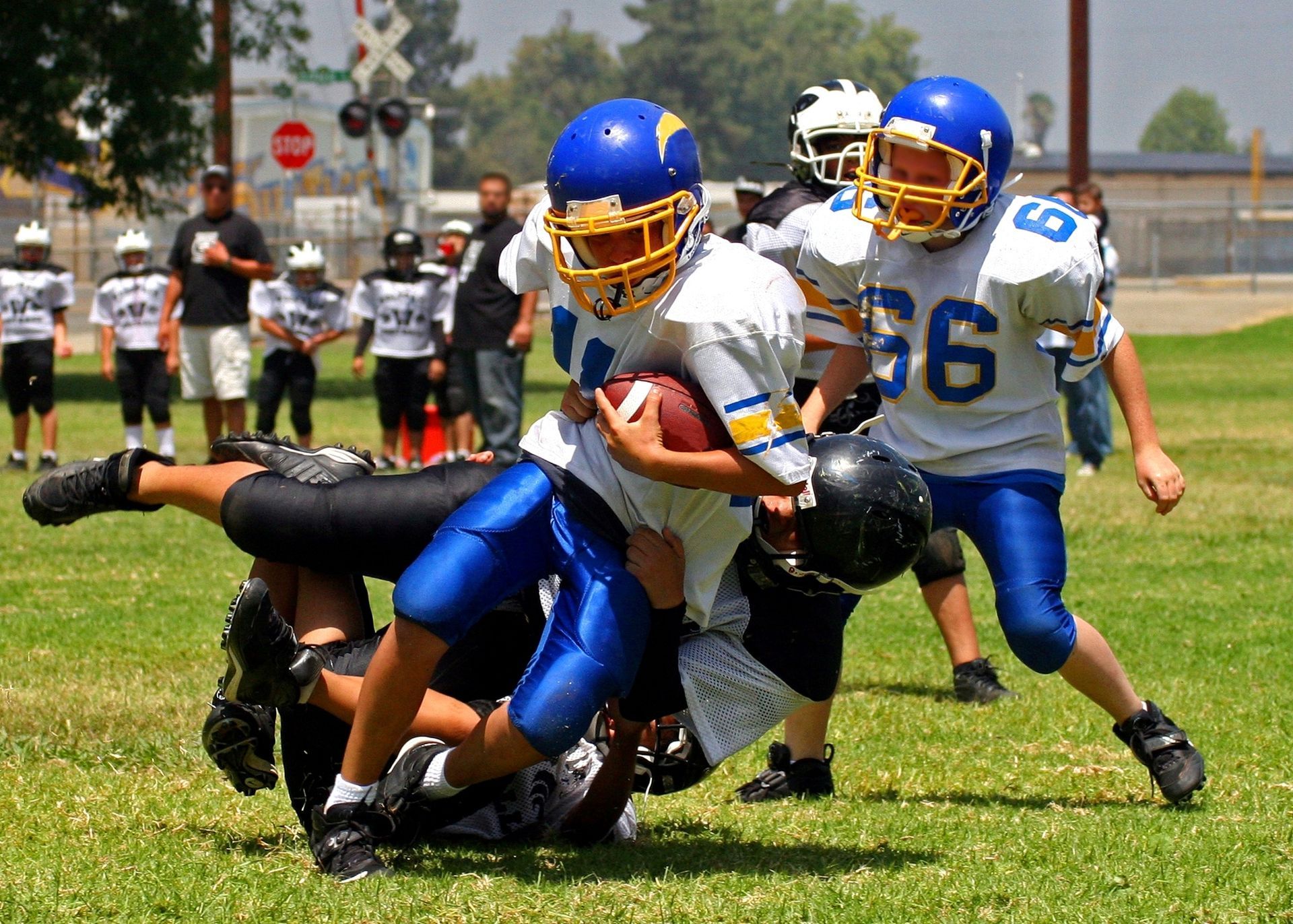 Youth football players in blue and white tackle a runner in black on a grassy field