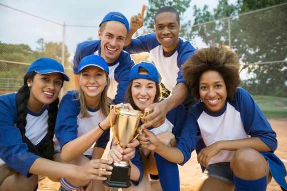 Softball team in blue and white uniforms celebrates with a trophy on a field.