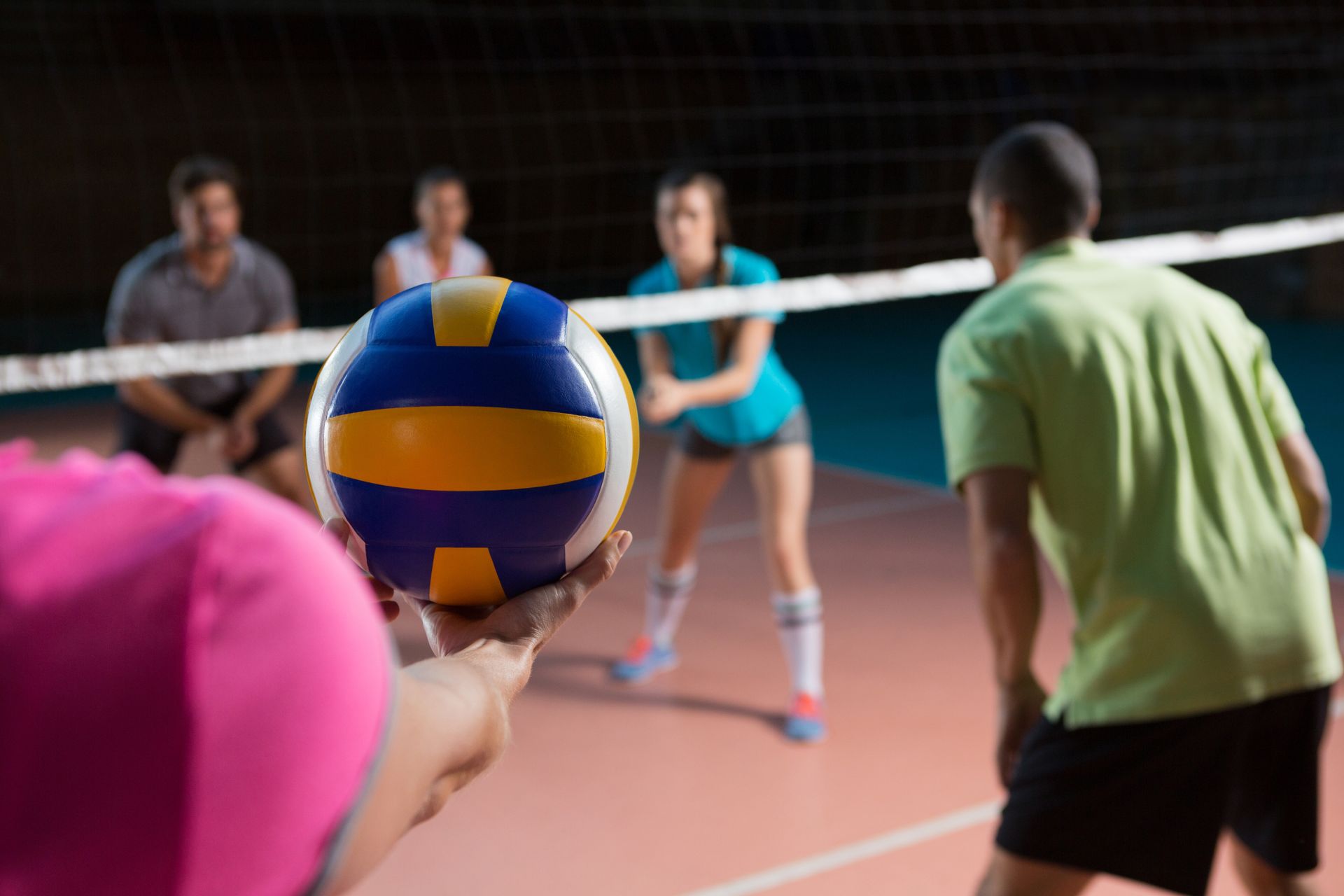 Volleyball game; player about to serve the ball, other players in position at the net.