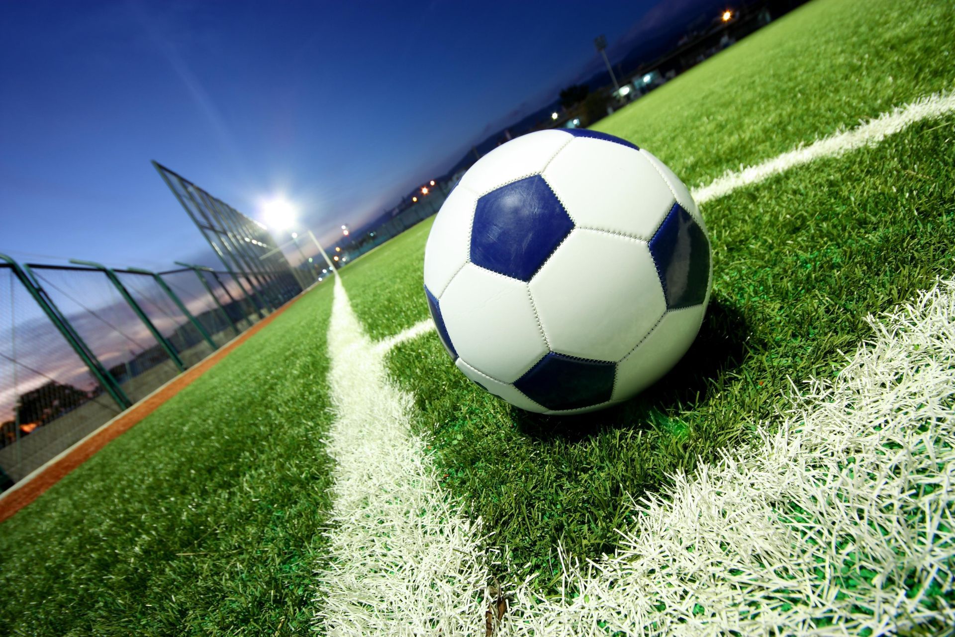 Soccer ball on the corner of a green soccer field with white lines, under stadium lights.