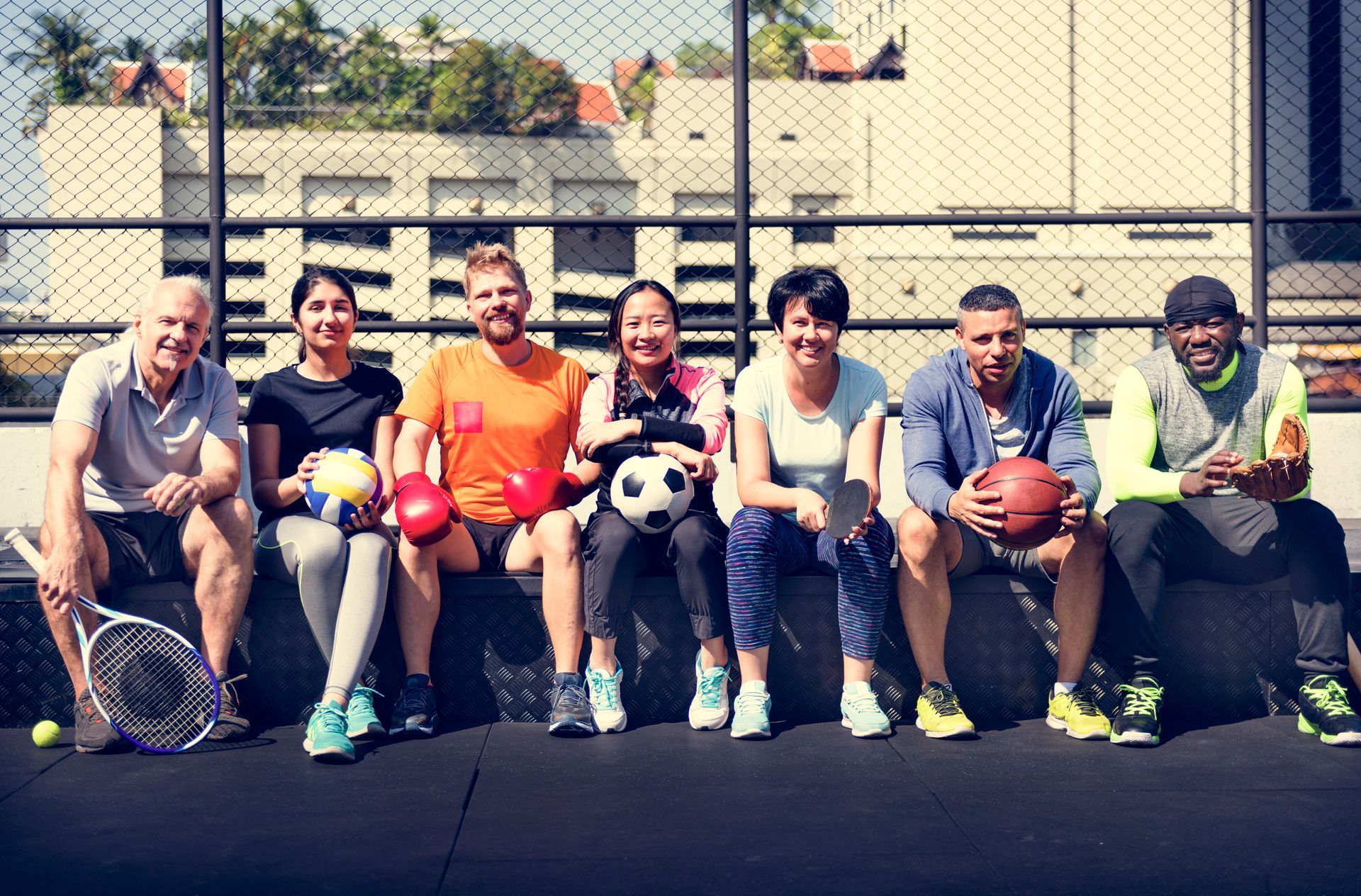 Group of people holding sports equipment, sitting on a rooftop, smiling.