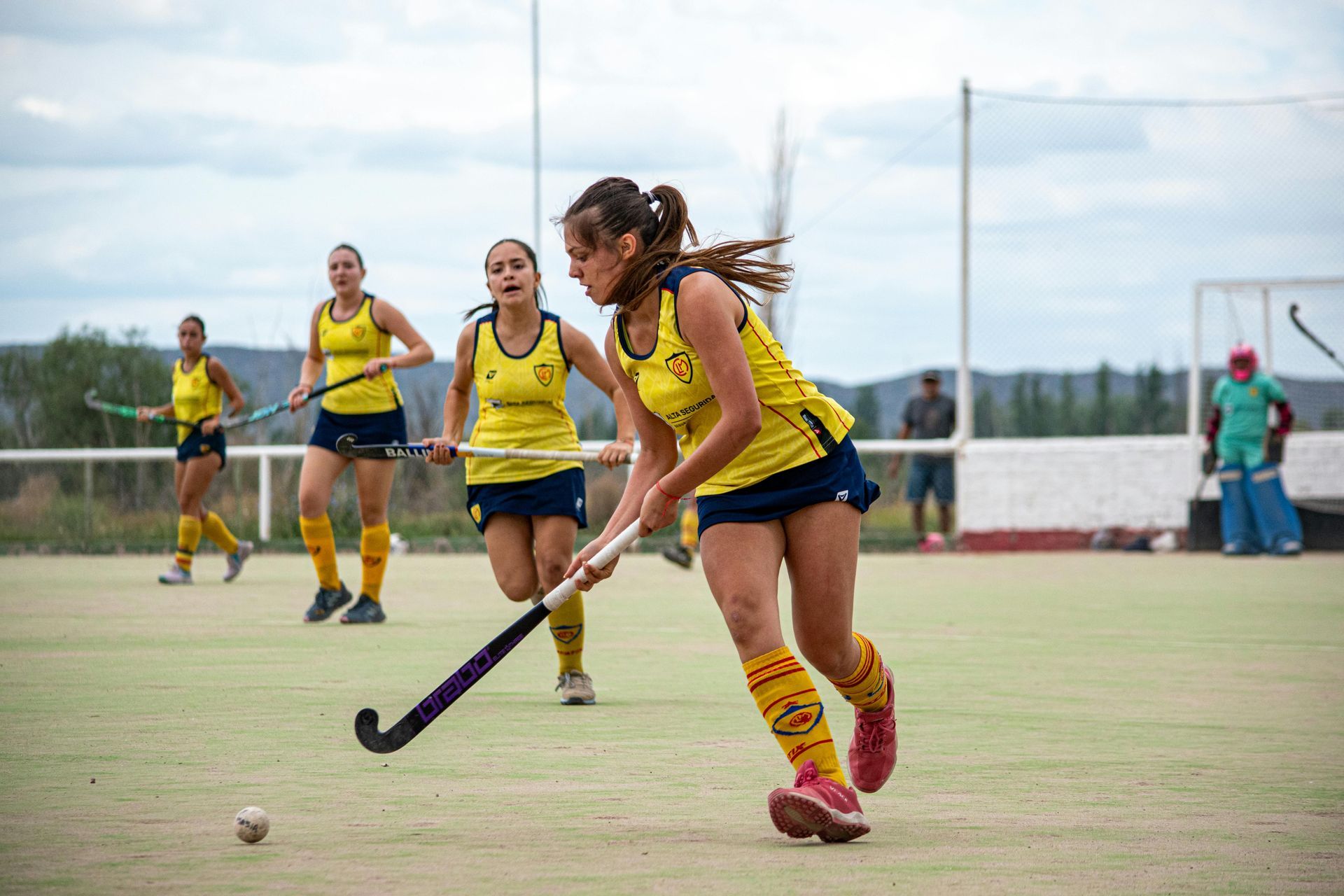 Hockey players in action near net: goalie in white, two attackers in blue and yellow. Ice, net.