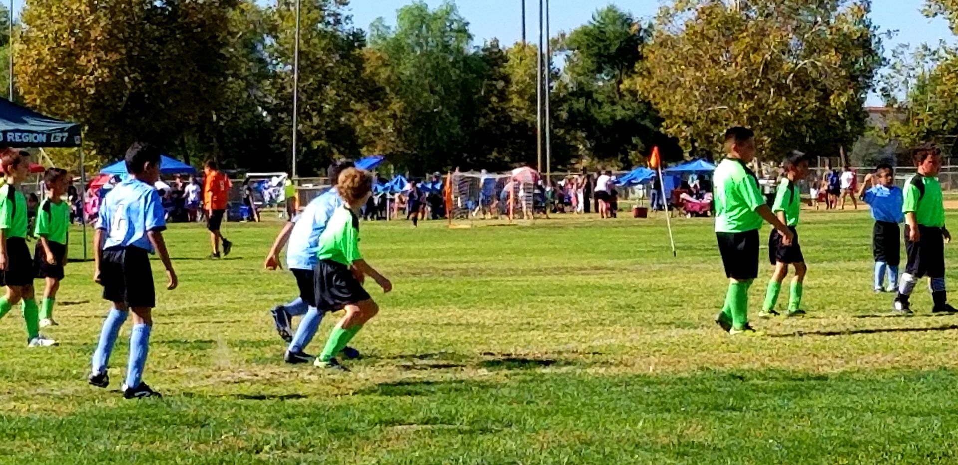 Soccer game on a grassy field. Players in light blue and green jerseys, black shorts, and green socks.