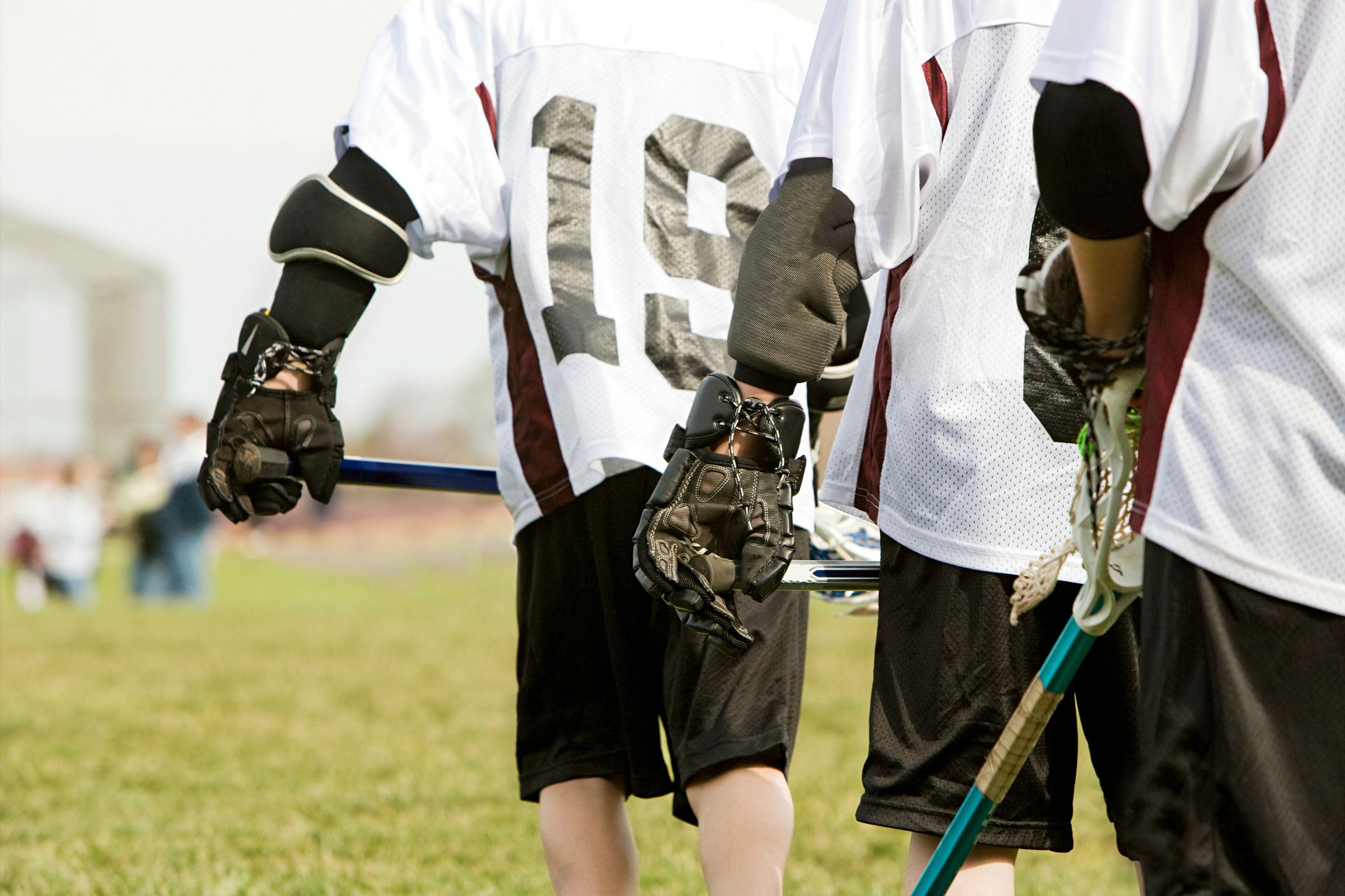 Lacrosse players in white jerseys with black shorts, holding sticks on a green field.
