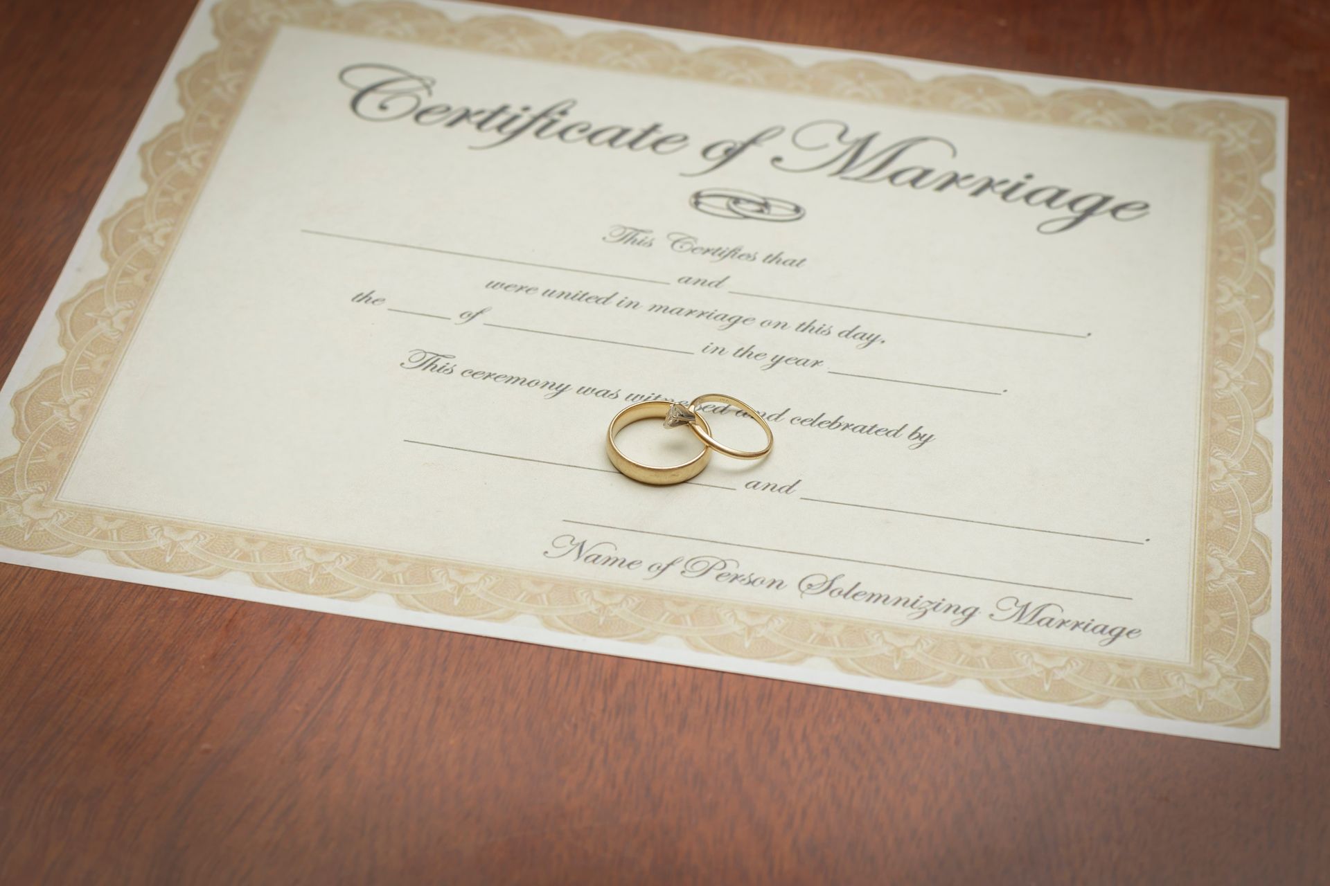 Marriage certificate with gold border and two wedding rings on a wooden table