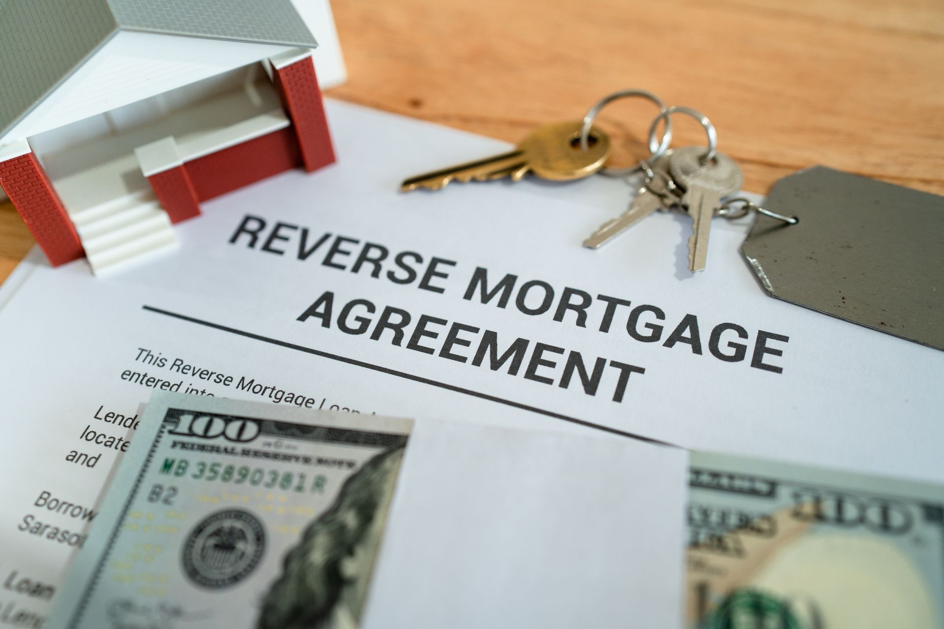 Reverse mortgage agreement with house model, keys, and dollar bills on a desk