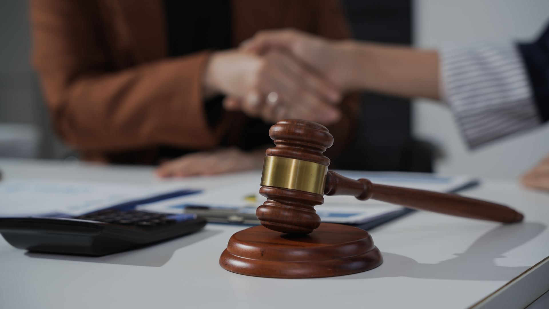 Handshake beside a judge’s gavel on a desk, suggesting a legal agreement or settlement