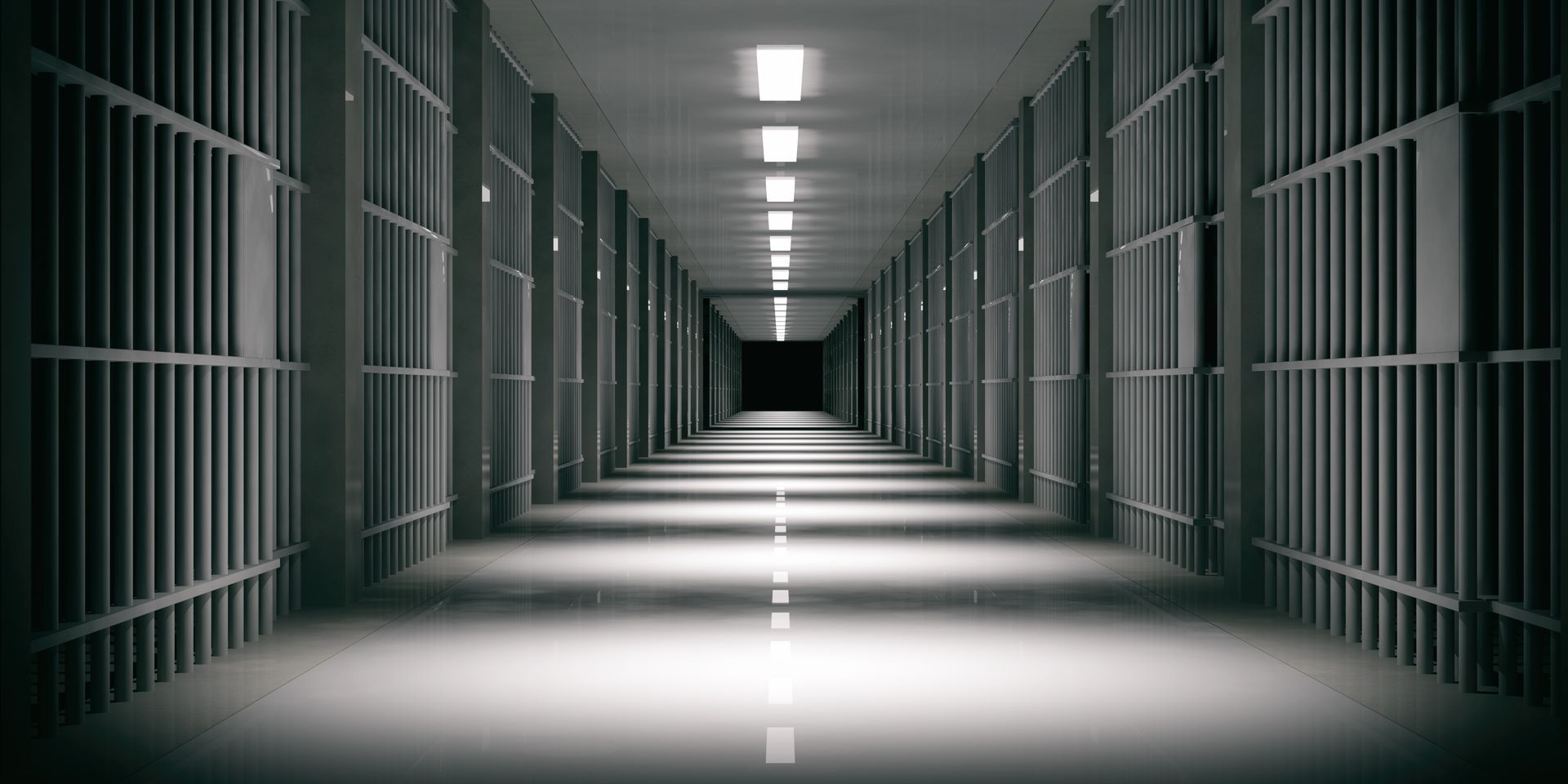 Empty prison corridor with barred cells on both sides, lit by overhead lights