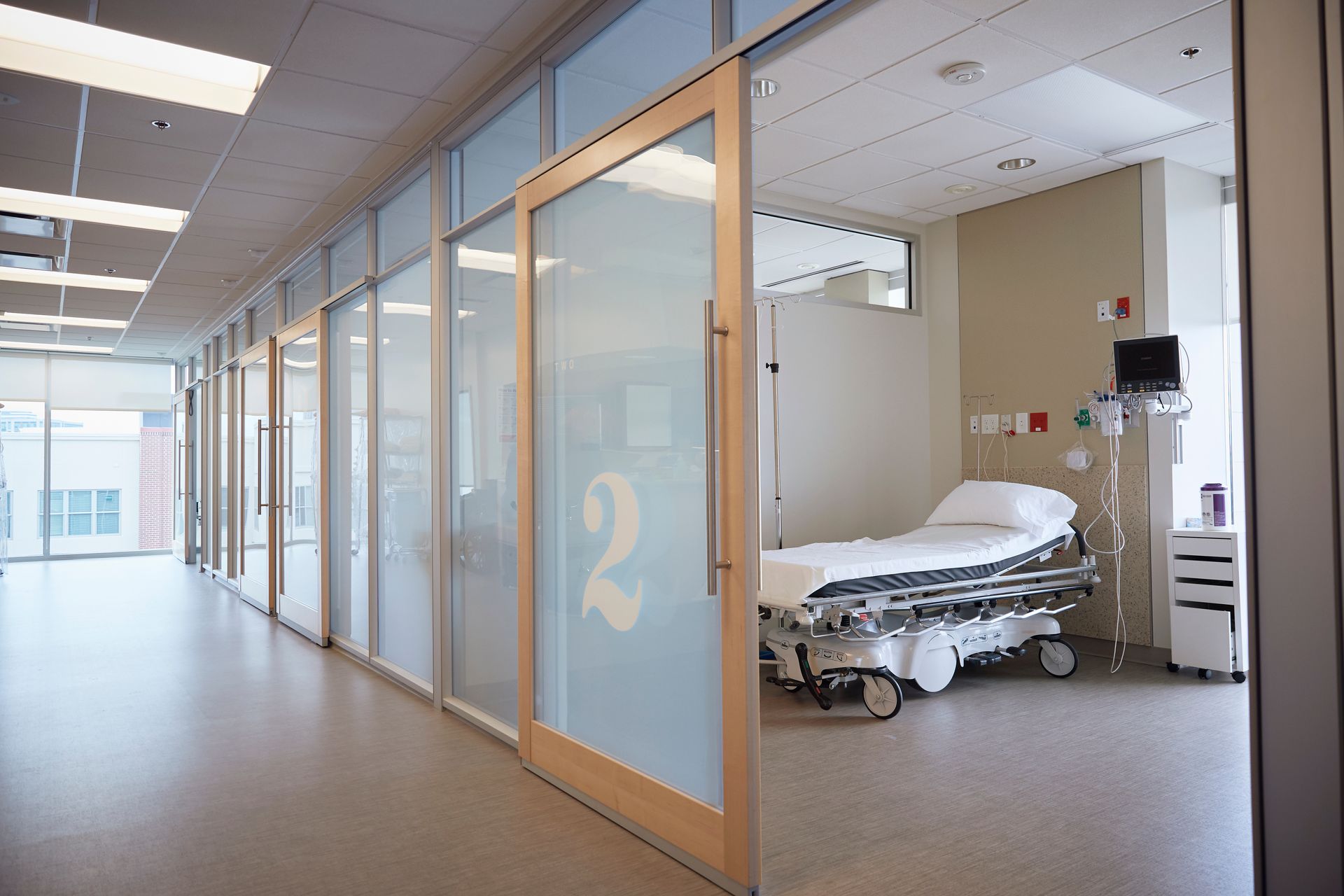 Hospital corridor with glass room doors and an empty patient bed inside a room