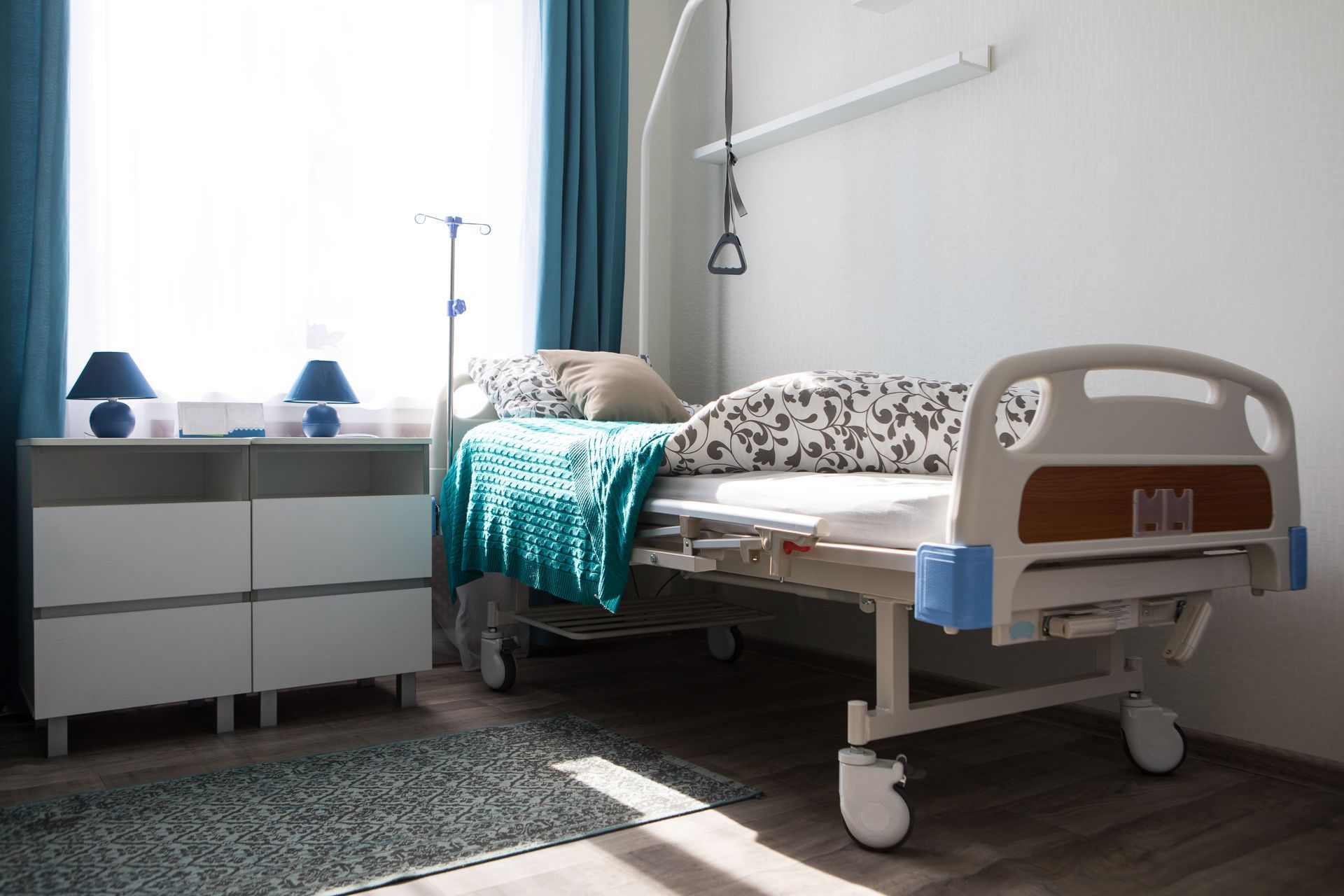 Modern hospital room with an empty bed, bedside table, window, and blue curtains