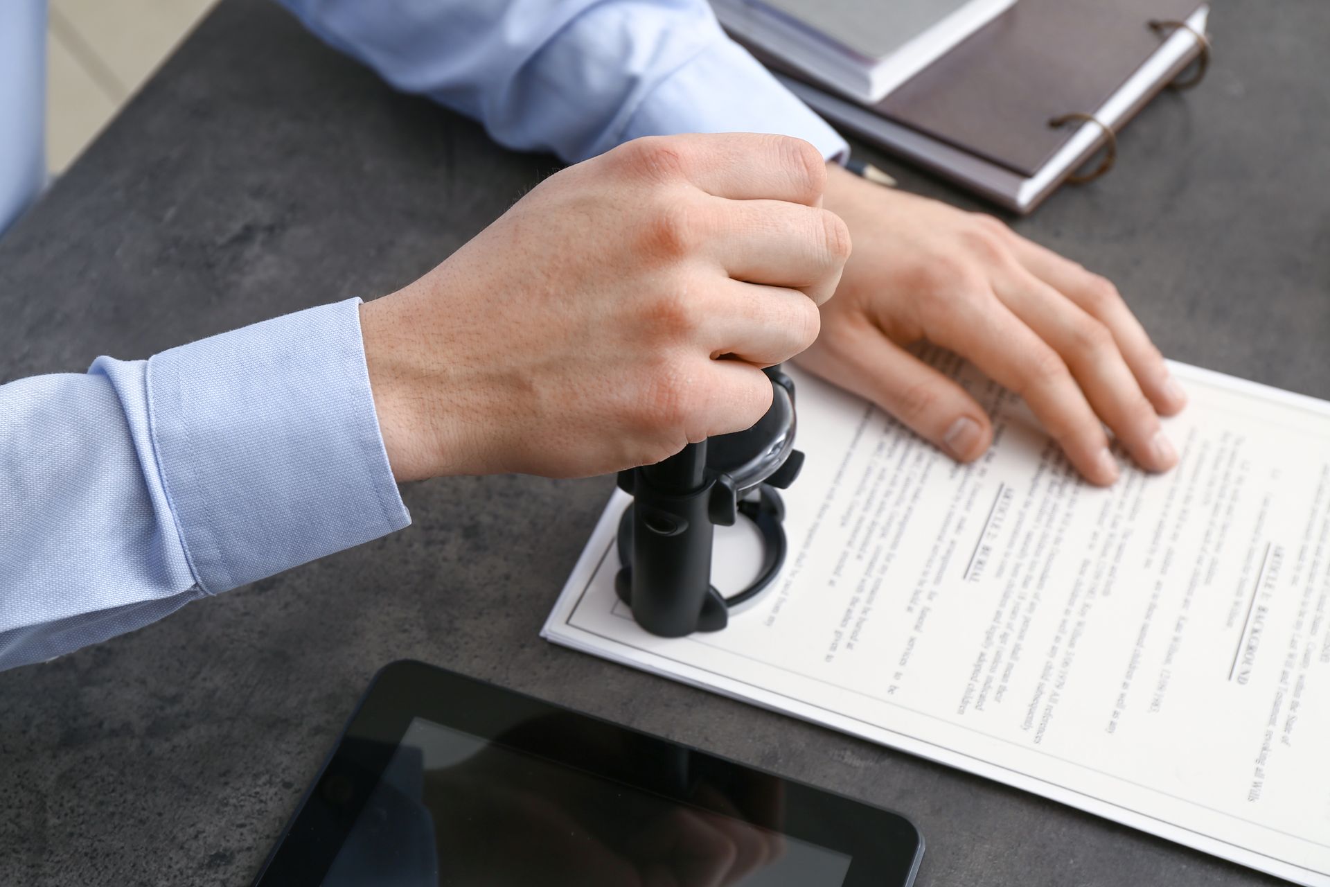 Hands stamping a document on a desk next to a tablet and clipboard