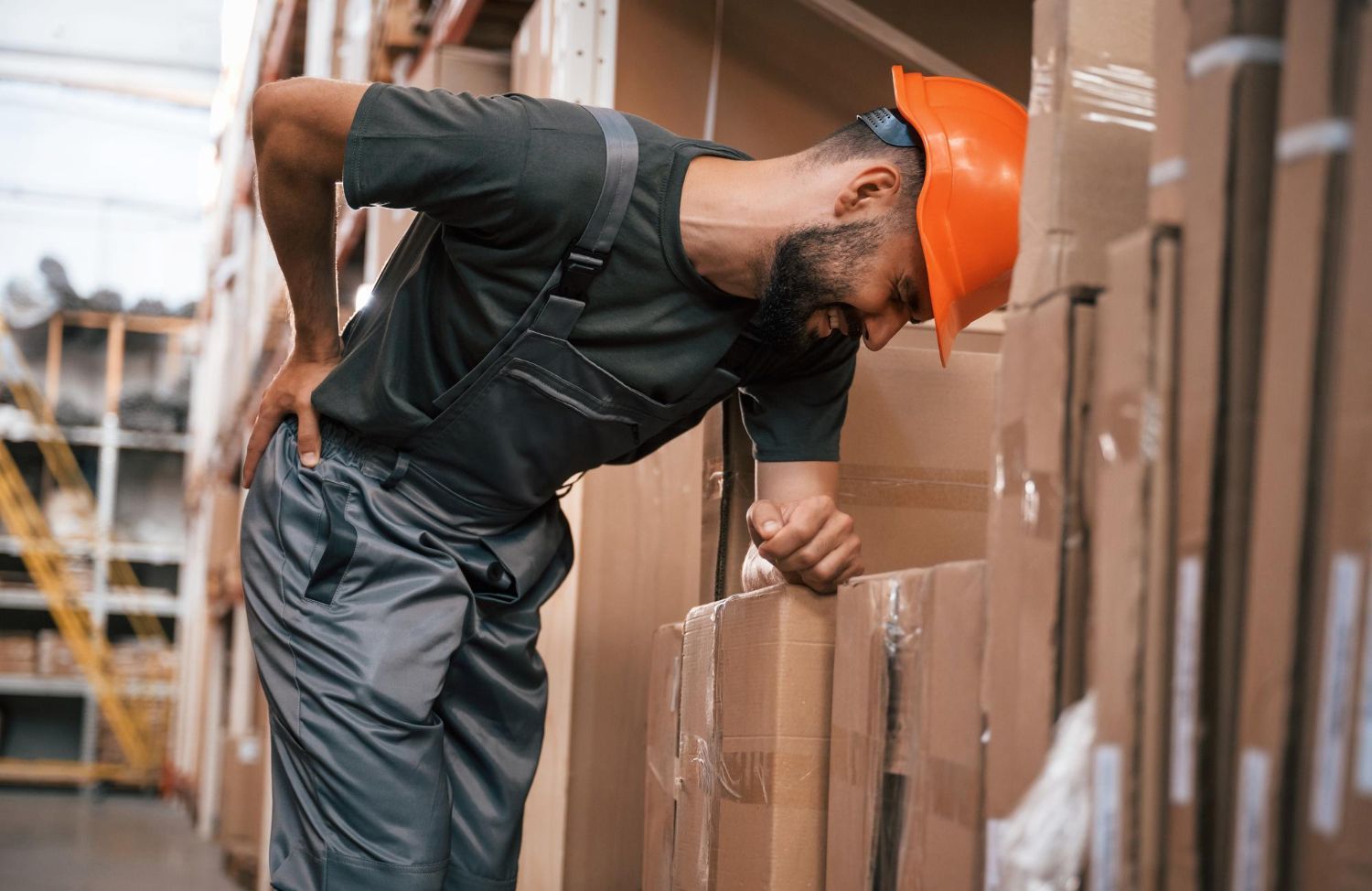 Warehouse worker hunched over boxes, holding back; possibly injured.