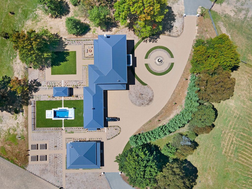 Aerial view of a house with a blue roof, pool, patio, circular driveway, and surrounding trees and lawn