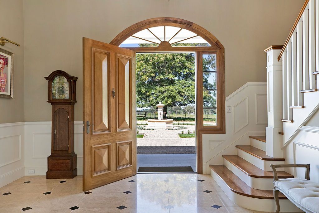 Front entry foyer with open wooden door, staircase, grandfather clock, and sunlight outside