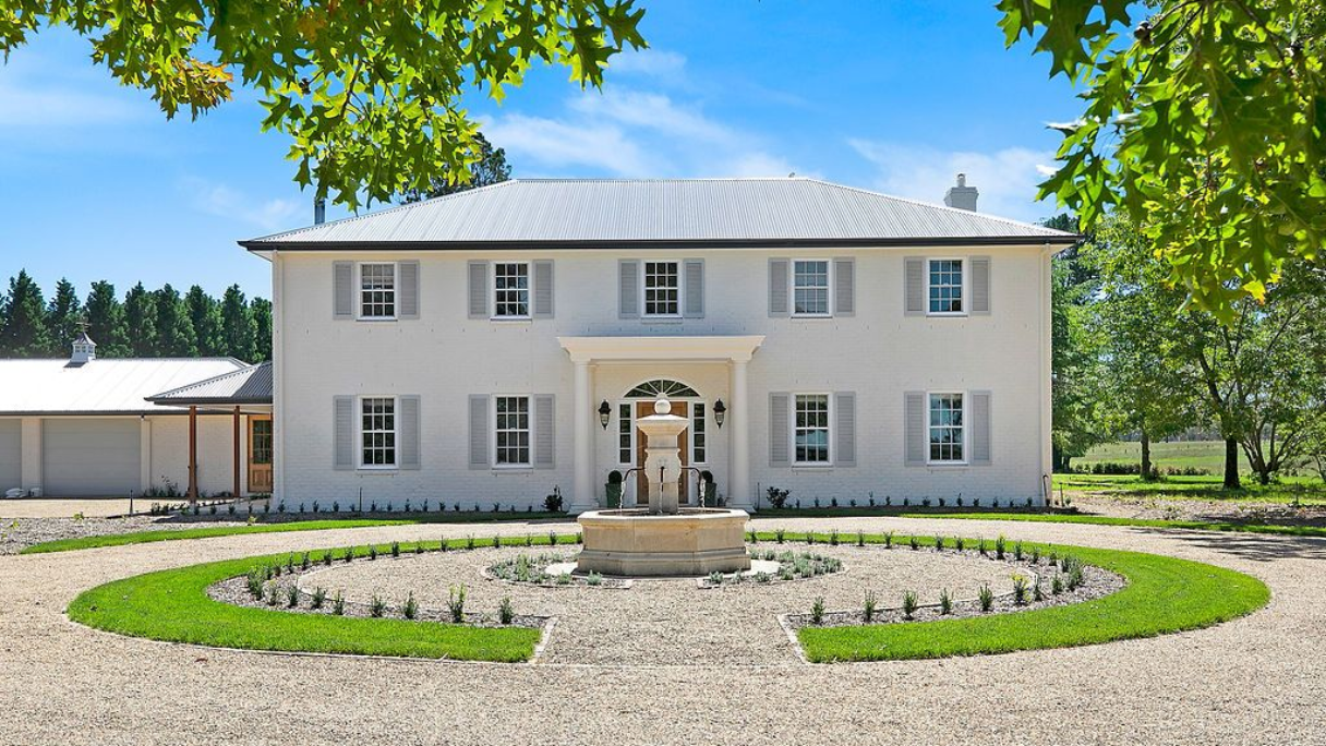 Large white two-story house with a circular gravel drive and landscaped front yard under a blue sky