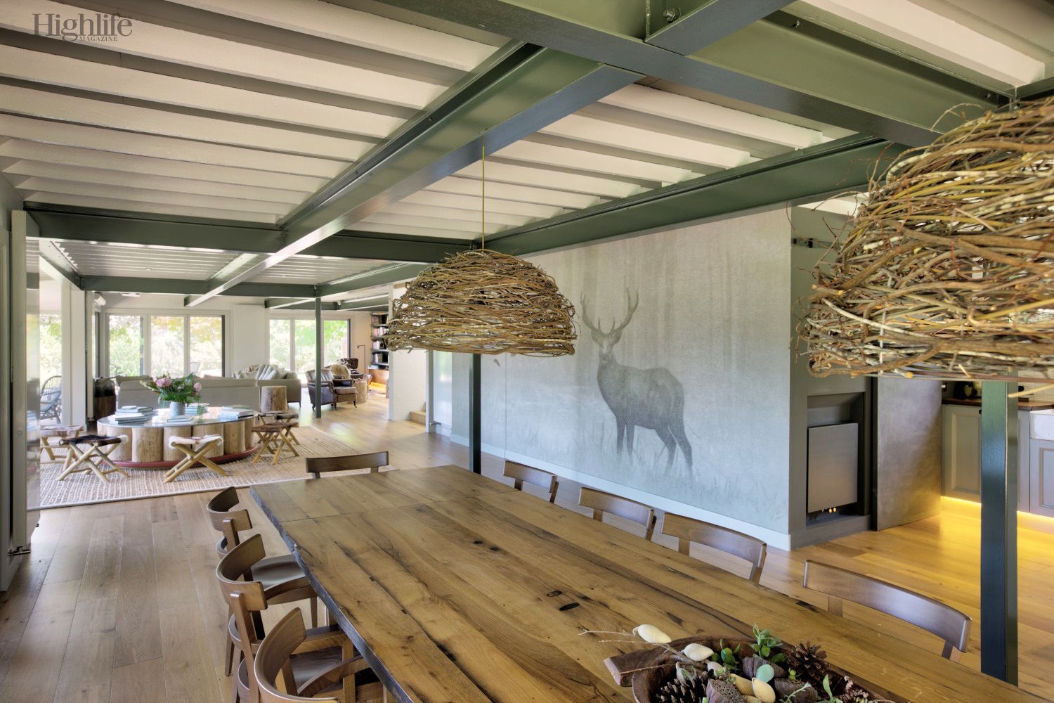 Rustic dining room with long wooden table, woven pendant lights, and wall mural of a deer