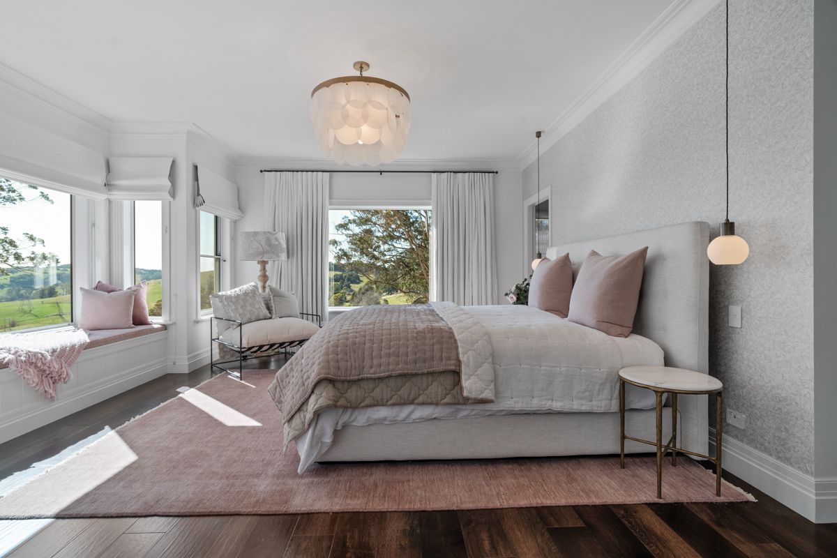 Bright bedroom with a bed, pink pillows, window seat, and large windows with sheer curtains.