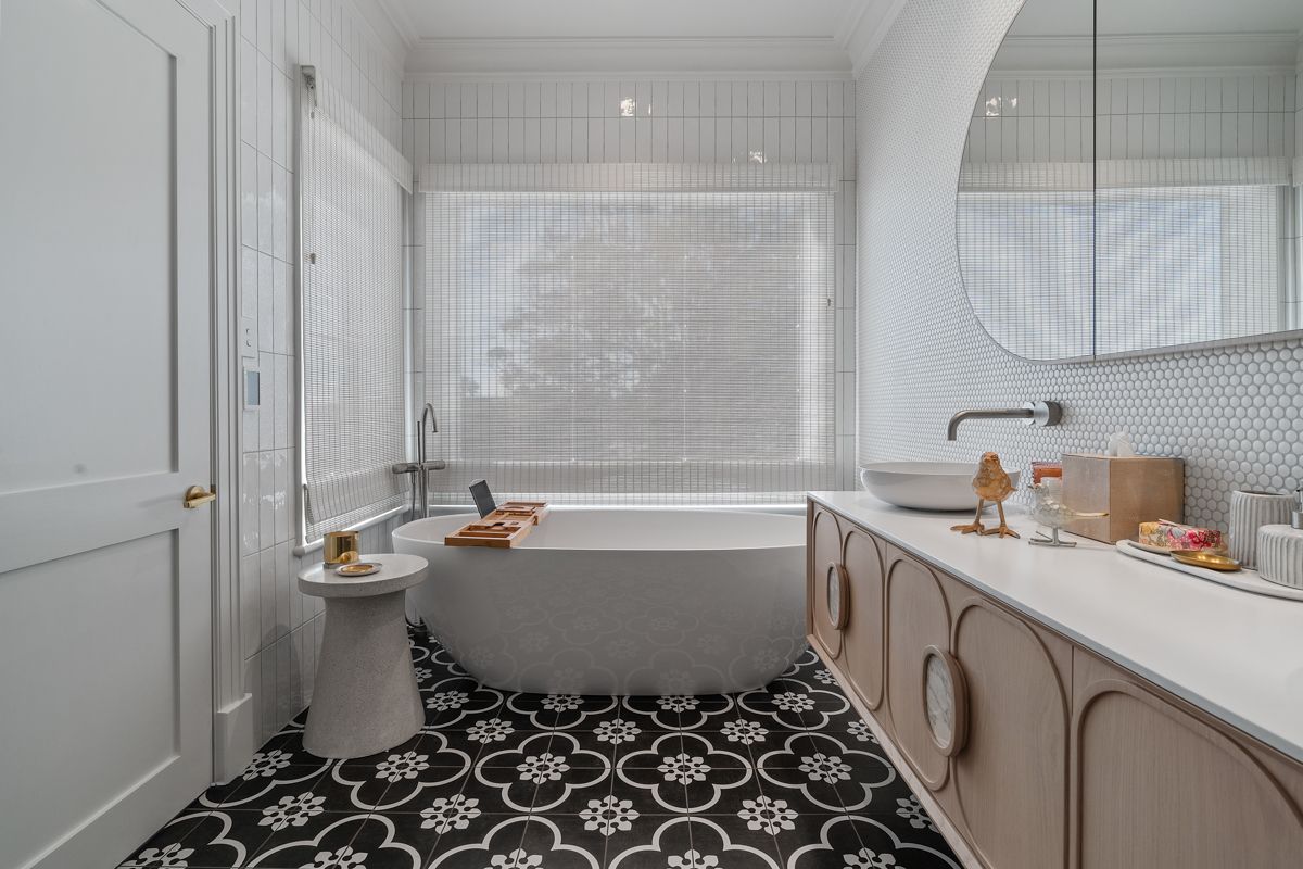 Bright white bathroom with freestanding tub, patterned black floor, and vanity by a large window