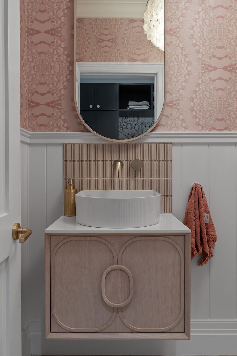 Pink and white bathroom vanity with round mirror, white sink, and coral towel hanging on the side