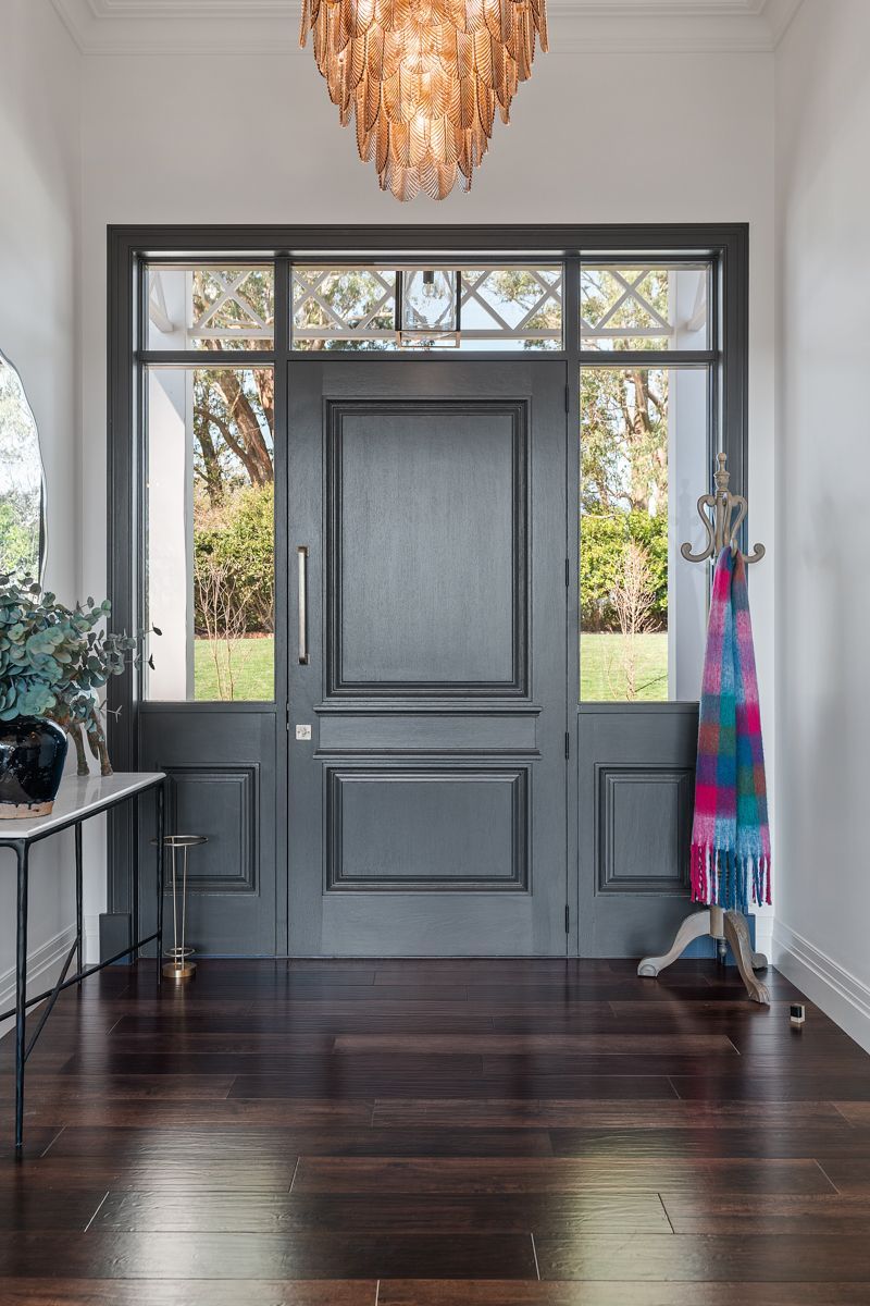 Front entryway with gray door, dark wood floor, and colorful coats on a hook beside a side table.