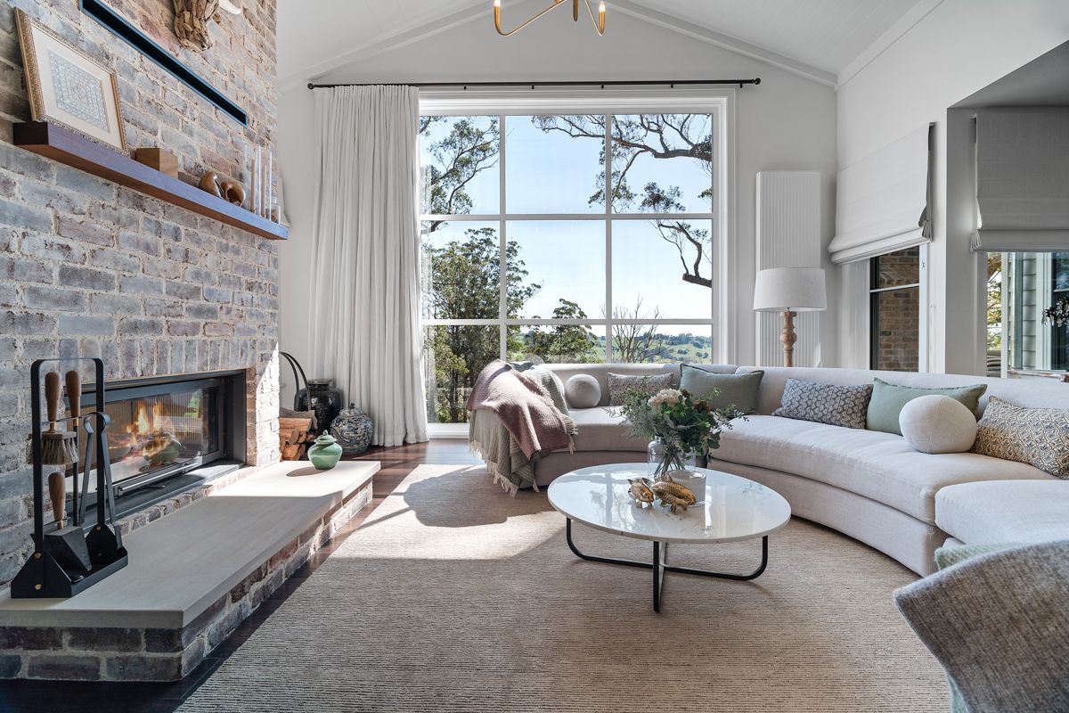 Bright living room with fireplace, white curved sofa, round coffee table, and large window with lake view