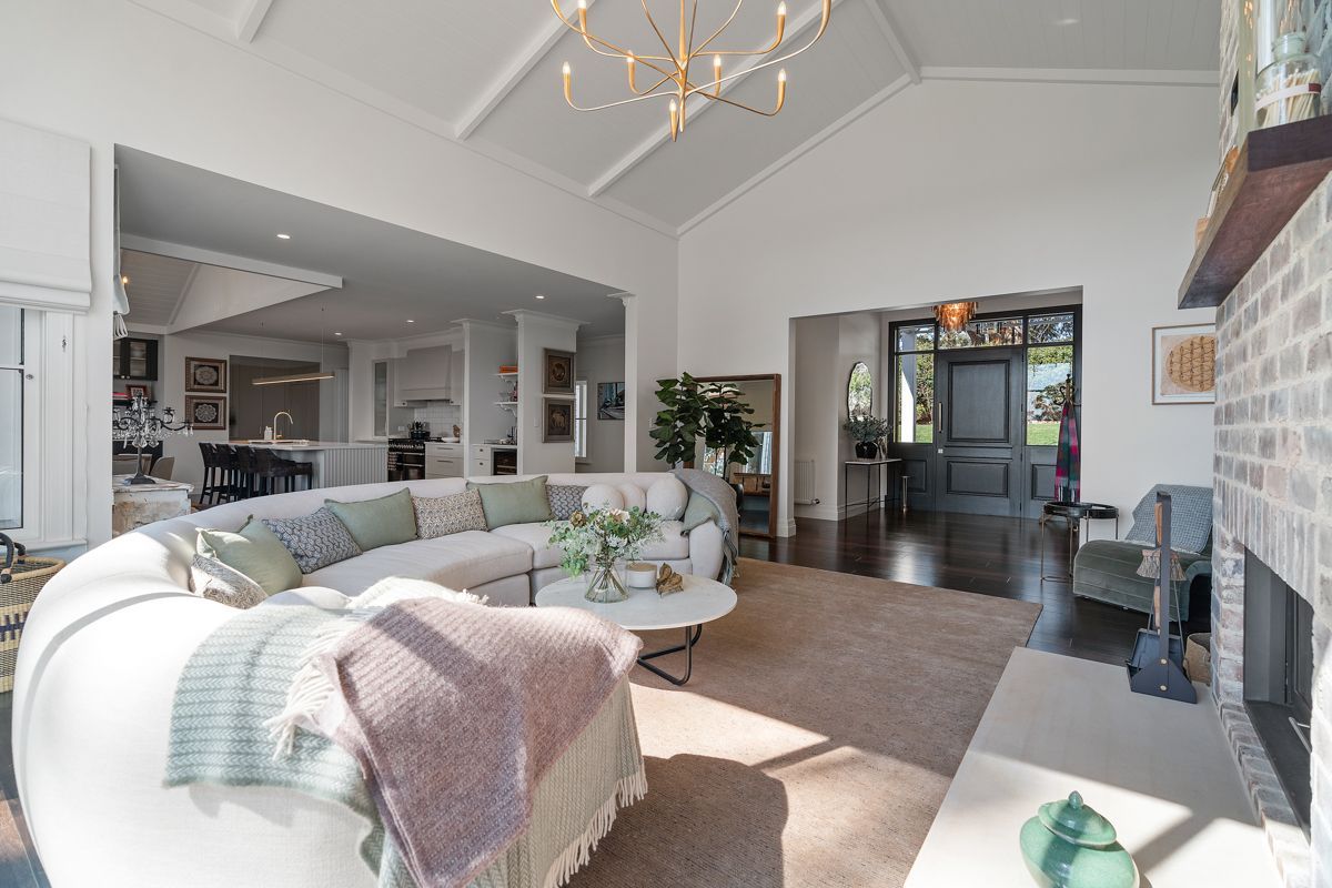 Bright living room with white sofa, fireplace, chandelier, and open view to kitchen and entryway