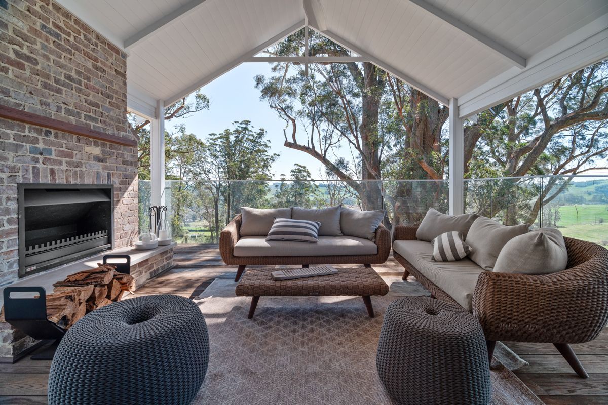 Covered outdoor patio with wicker seating, fireplace, and forest view