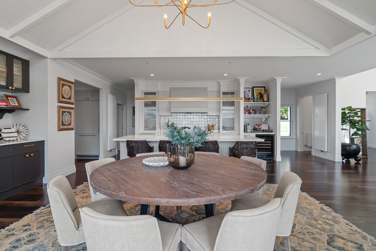 Bright dining room with round wood table, upholstered chairs, and built-in shelves facing a windowed living area