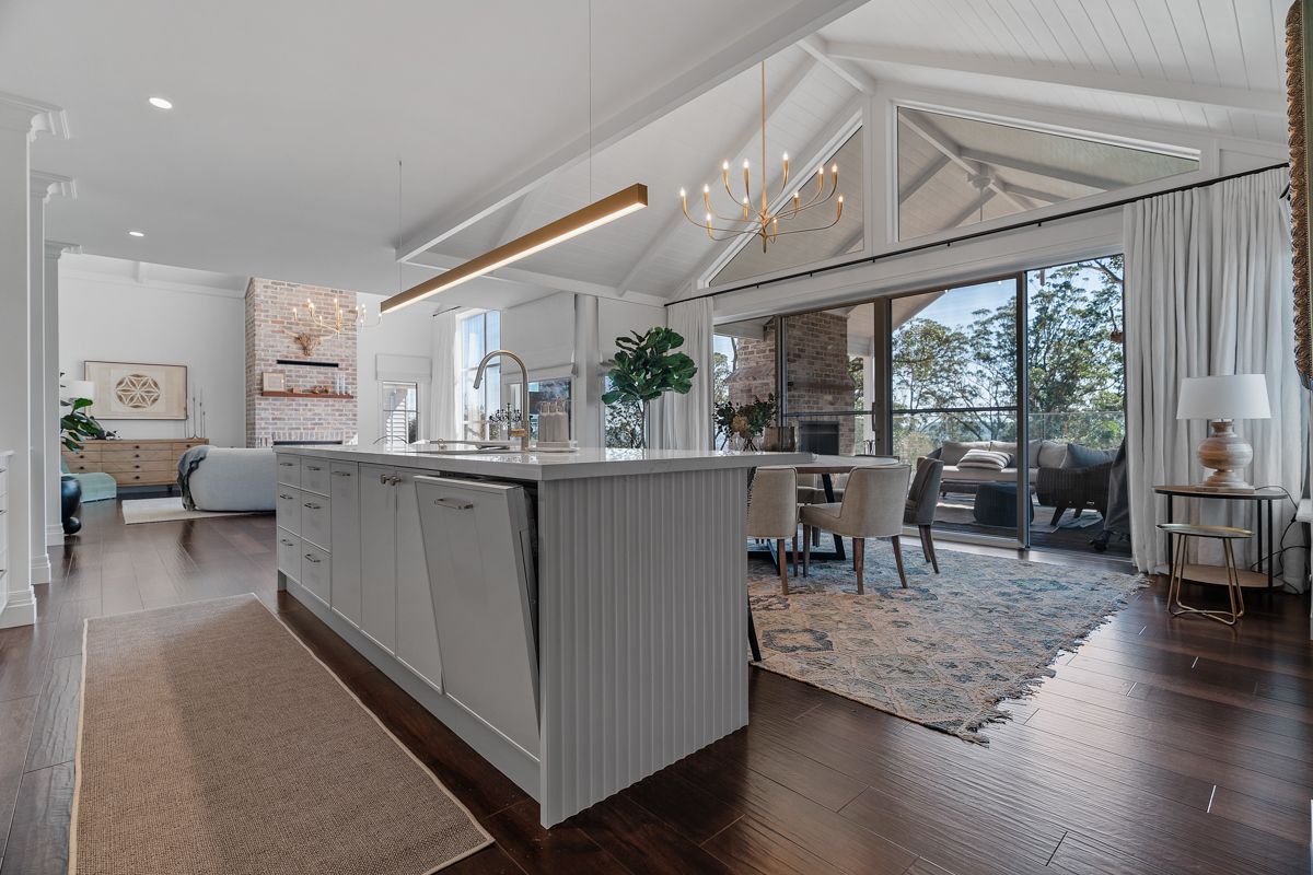 Bright open-plan kitchen and dining area with white cabinetry, wood floors, and a view of trees outside.