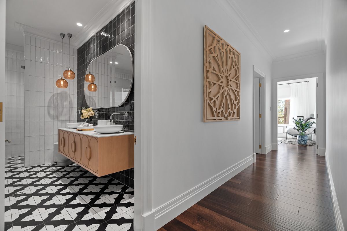 Modern hallway leading to a bathroom with black-and-white patterned tile and wood vanity, bright white walls