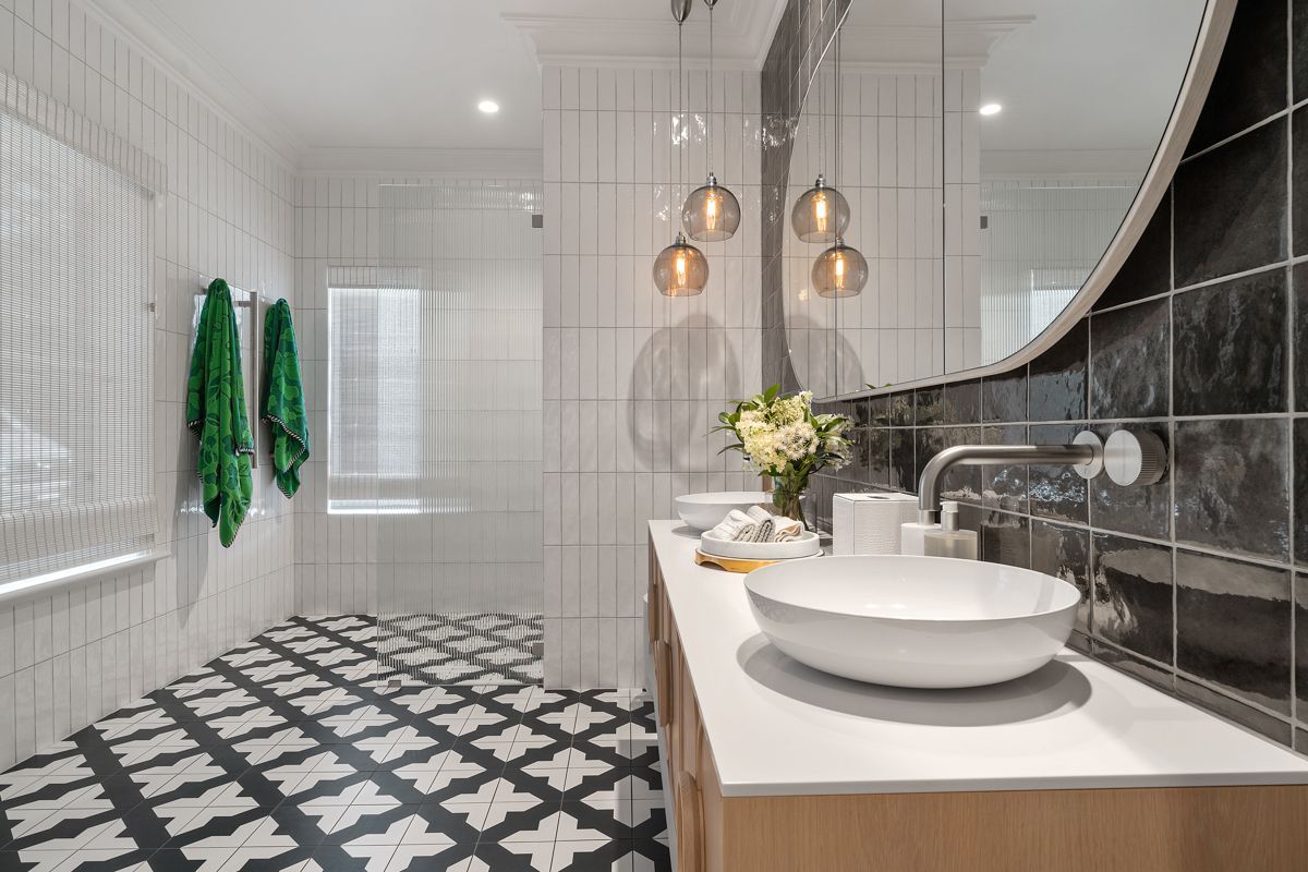 Modern bathroom with patterned black-and-white floor, white vanity, vessel sinks, and copper pendant lights