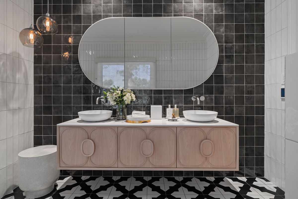 Modern bathroom vanity with twin sinks, round mirror, dark tiled wall, and geometric black-and-white floor
