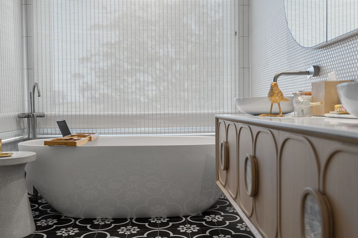 Modern bathroom with freestanding tub, patterned black-and-white floor, and vanity sink by a window