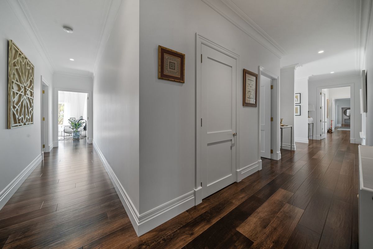 Bright modern hallway with dark wood floors, white walls, framed art, and doors leading to a distant room