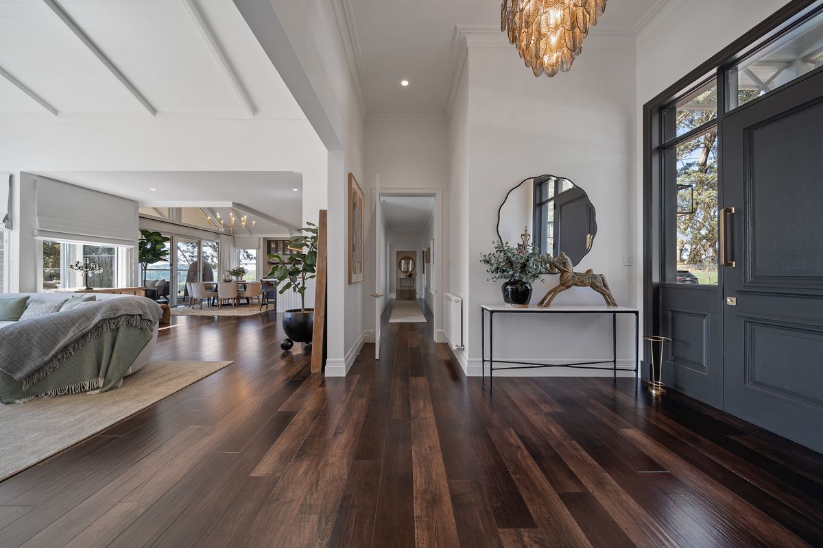 Modern foyer with dark wood floors, white walls, chandelier, round mirror, and a black front door.