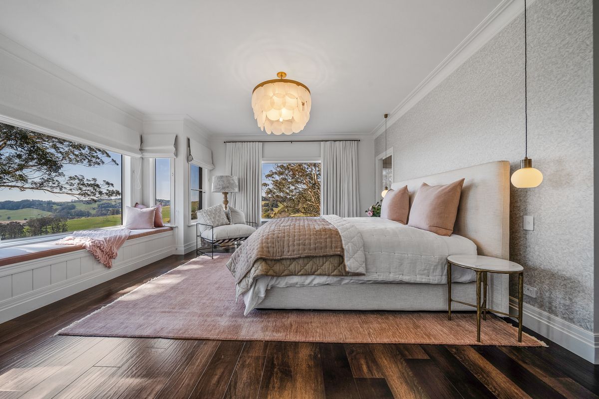 Bright modern bedroom with large windows, white walls, wood floors, and a bed with neutral bedding.