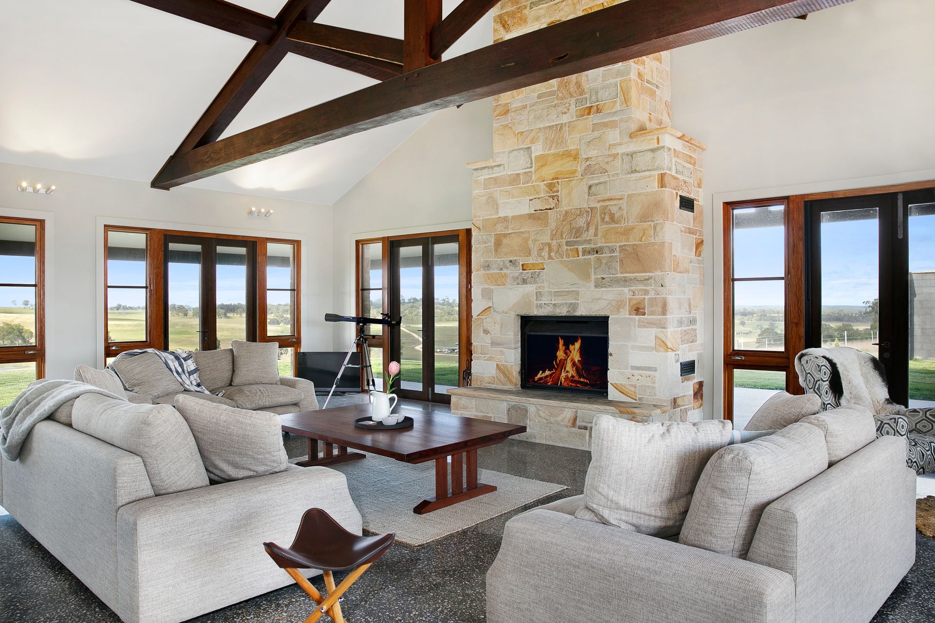 Spacious living room with stone fireplace, exposed beams, and large windows overlooking a view